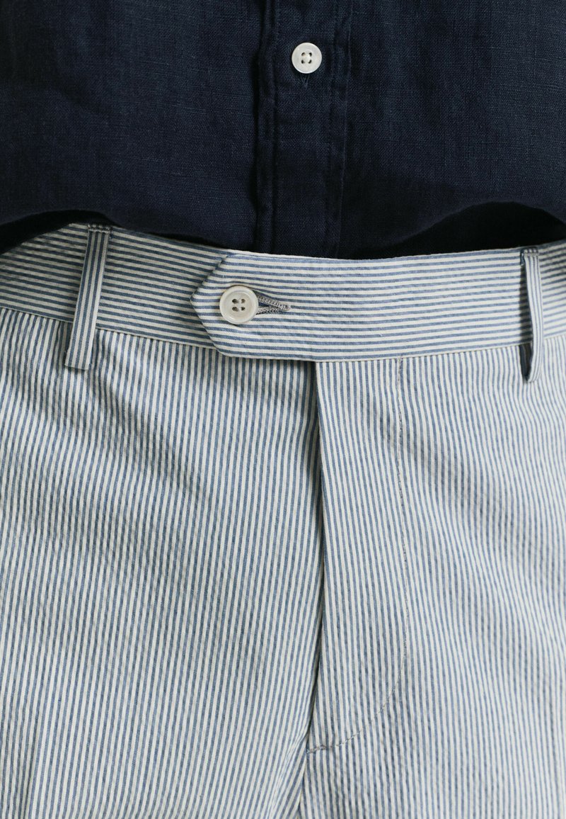 Los pantalones de algodón a rayas presentan un patrón en azul claro y blanco, con una parte delantera plana y un cierre de botón con un lazo para el cinturón. Tejido texturizado.
