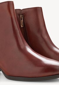 Brown leather ankle boots with a glossy finish, featuring a side zipper and a tapered toe. The heel is approximately 3 inches.