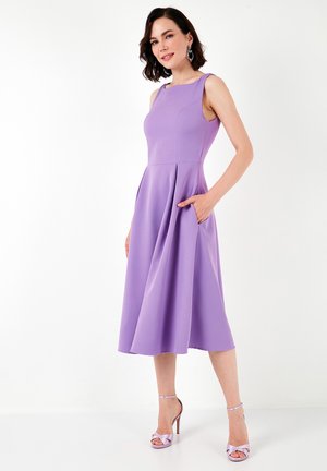 Hihaton violetti mekko, jossa on istuva yläosa, levenevä hame ja taskut. Sujuva kangas, jossa on hienovarainen kiilto. Yhdistetty laventelin värisiin korkokenkiin.