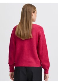 Fuksijas adīta džempera ar garām piedurknēm un ribinātiem rokturiem. Strukturēts priekšpuse un vienkrāsaina aizmugure. Ar apaļu kakla izgriezumu un brīvu piegriezumu.