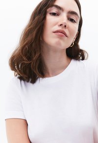 T-shirt bianca in cotone con scollatura rotonda e maniche corte. Texture liscia con una forma aderente. Design minimalistico, senza motivi o dettagli.