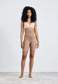 Beige bh med en jevn overflate og justerbare stropper, kombinert med høyt midjefordelt, hudfarget shorts i et elastisk stoff.