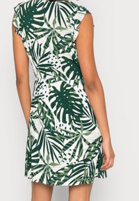 Robe courte verte et blanche avec un motif de feuilles tropicales, des manches volantes et une taille élastique pour un ajustement décontracté.