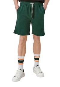 Shorts en polaire verte avec une ceinture élastique et un cordon blanc ; dotés de poches latérales et d'un détail logo ; portés avec des chaussettes rayées et des baskets blanches.