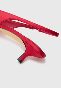 Rød satin slingback hæl med spidse tå, tynd rem og lav sort blokhæl. Glat tekstur med synlige syningsdetaljer.