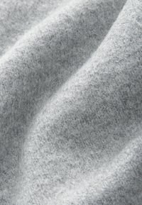Tessuto grigio chiaro e morbido con una trama testurizzata, caratterizzato da piccole fibre irregolari per un aspetto accogliente. Adatto per abbigliamento o tessuti per la casa.