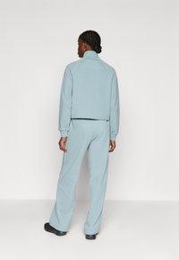 Lys blå, kort fleecejakke med høy krage, ribbede mansjetter, og matchende joggebukser. Glatt tekstur, enkel design med subtil sømdetalj.