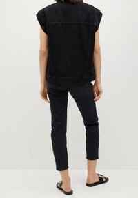 Chaleco de mezclilla negro con mangas enrolladas, combinado con jeans negros de corte slim y sandalias negras. Diseño sencillo, bordes limpios y sin adornos visibles.