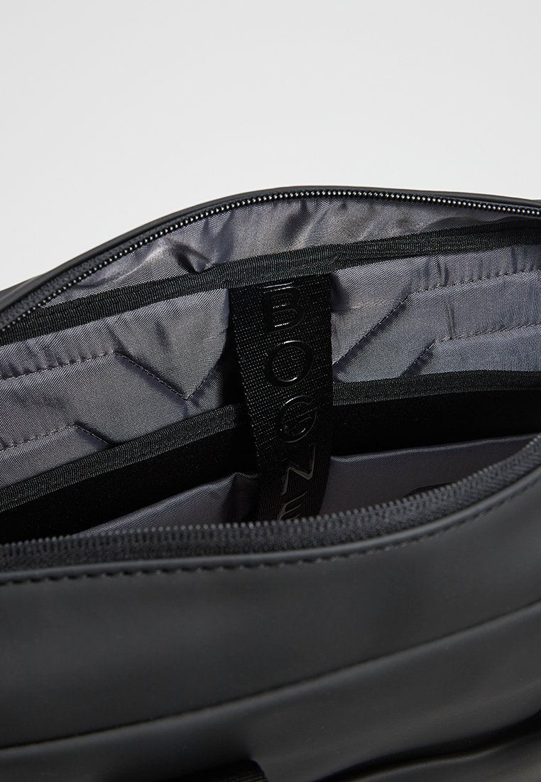 Schwarze Tasche mit Reißverschluss, innen mit glatter Textur, grauem Futter und einem BOGNER-Logo-Gurt. Verfügt über unterteilte Sektionen.