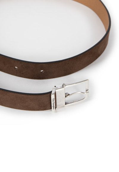 Brązowy pasek zamszowy z srebrną metalową klamrą. Posiada gładkie wykończenie i kilka otworów do regulacji rozmiaru na całej długości.