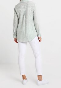 Hellgrünes Langarmhemd mit weißen senkrechten Streifen, mit einem Button-Down-Kragen und einem gefältelten Rücken. Kombiniert mit weißen Skinny-Jeans und Turnschuhen.