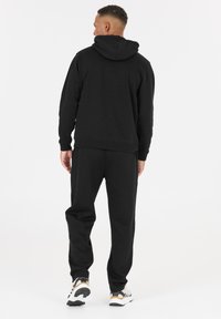 Zwarte hoodie en joggingbroek set gemaakt van een katoenen mixstof, met een relaxte pasvorm, ribgebreide boorden en een capuchon. Schoeisel bestaat uit witte sneakers.