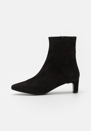 Bottine en cuir suédé noir avec un bout pointu et un petit talon carré. L'empeigne présente une texture lisse et une silhouette épurée.