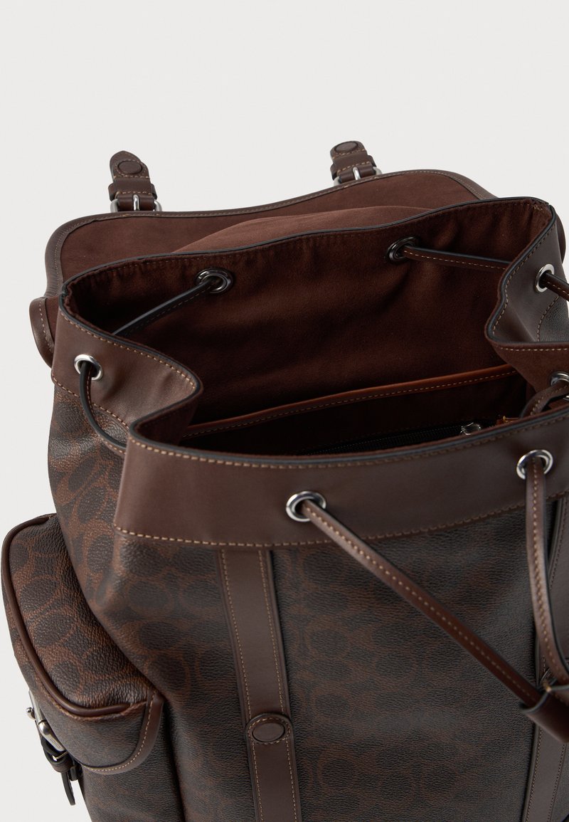 Brown leather backpack with a textured pebbled surface and smooth accents. Features drawstring closure and contrasting lighter stitching.