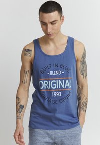 Modrá tielko s okrúhlym výstrihom s nápisom 'Built in Blue Blend Original Vintage Denim 1993' v tučnej typografii. Bavlnený materiál.