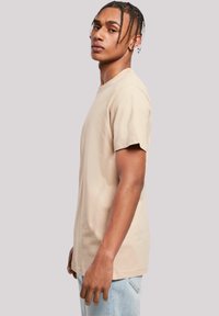 Beige cotton t-shirt with short sleeves, crew neck, and a relaxed fit. Model stands sideways, showcasing simple design and smooth texture.