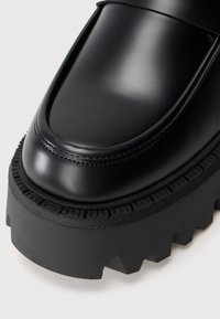 Melnas ādas loafers ar spīdīgu apdari, piedāvājot masīvu gumijas zoli ar teksturētu saķeri un rievotām malām. Gluda virsmas apdare.