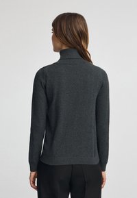 Pull col roulé gris en matériau doux, doté de manches longues et d'un design ajusté. L'arrière présente une texture lisse et un ourlet droit.