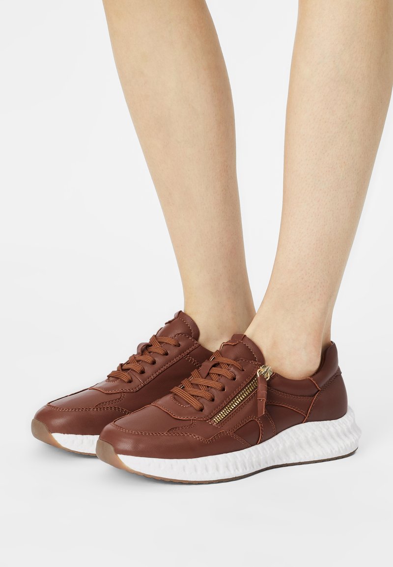 Brown leather sneakers with a textured upper, featuring lace-up closure, a decorative side zipper, and a white cushioned sole.