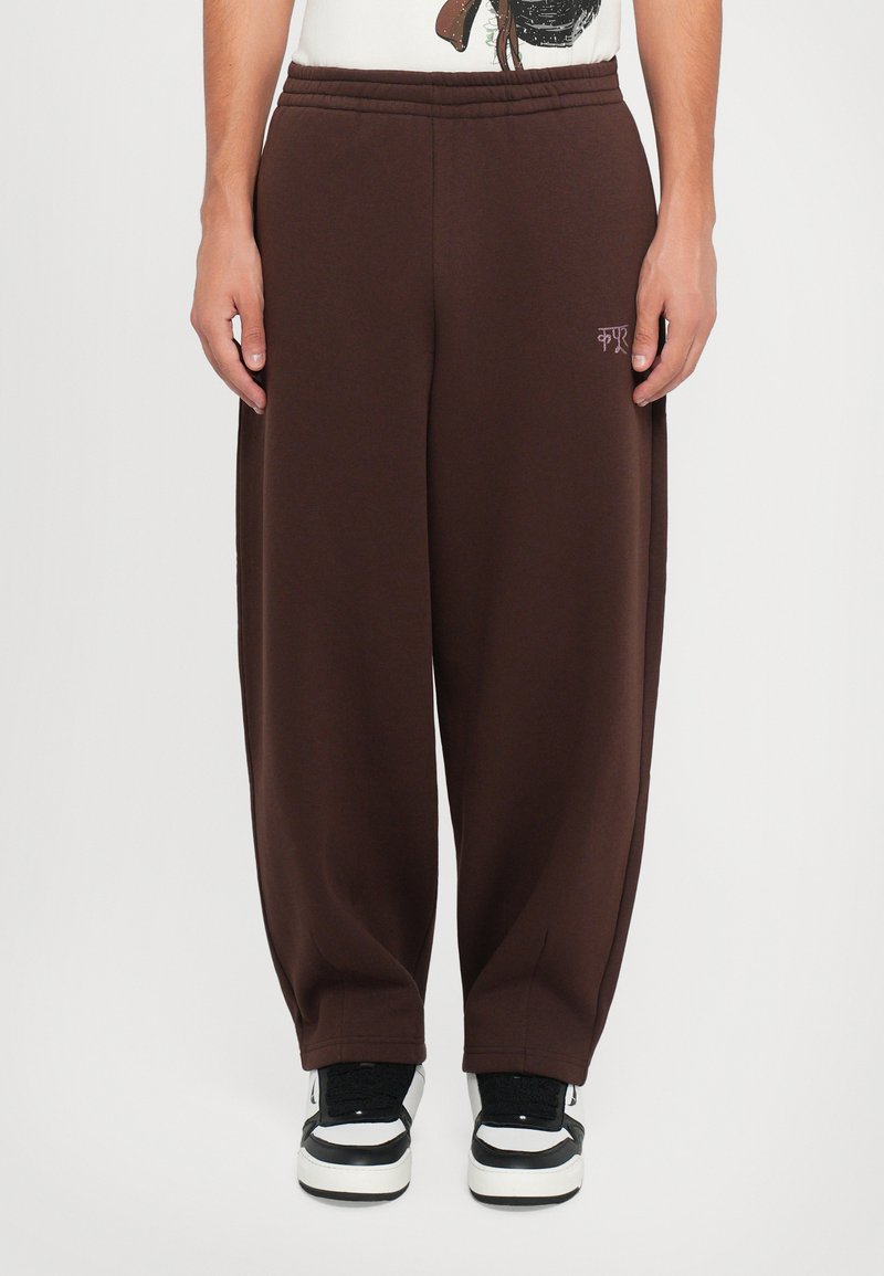 Brown sweatpants with an elastic waistband, tapered legs, and side pockets. Features a small logo embroidered on the upper left leg.