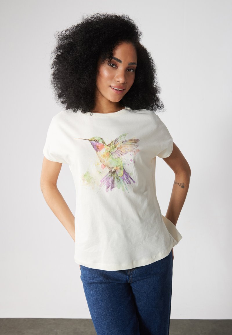 Krämfärgad bomulls-T-shirt med en färgglad akvarelldesign av en kolibri på framsidan. Rund halsringning och korta ärmar, avslappnad passform.