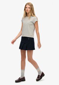 T-shirt grigia a maniche corte, gonna a pieghe blu scuro con righe inglesi, calze a strisce grigie e beige, e mocassini marroni scuri. Abbigliamento semplice e casual.