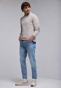 Suéter de lana gris claro, jeans de mezclilla azul y zapatillas deportivas beige. El suéter tiene un cuello redondo y un acabado texturizado. Corte casual.
