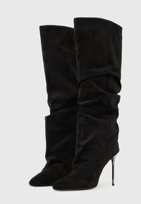 Botas altas hasta la rodilla de ante negro con diseño deshilachado, punta puntiaguda y tacón alto delgado. Textura suave con pliegues sutiles para mayor detalle.