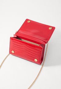 Borsa a tracolla in finta pelle rossa con texture coccodrillo, accessori in oro e tracolla a catena. Apertura con due chiusure a scatto magnetiche.