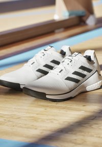 Weiße Sportschuhe mit schwarzen Streifen, strukturiertem Obermaterial, runder Zehenpartie und Gummisohle. Schnürsenkel und gepolsterter Schaftrand sichtbar.