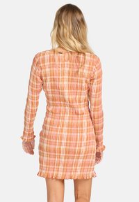 Robe à manches courtes en tissu doux et texturé avec un motif à carreaux pêche et rose. Elle a une taille cintrée et un ourlet froncé.