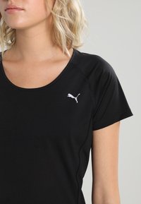 Woman with blonde hair wearing a black Puma short-sleeve shirt with a round neckline and visible Puma logo on chest.