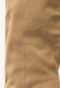 Tan suede material with a soft texture, featuring a pronounced seam running vertically along the side.