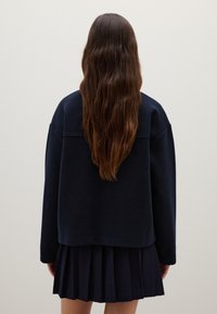 Navy blue oversized sweater with a boxy shape, long sleeves, and ribbed texture, paired with a pleated navy skirt.