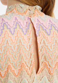 Spitzenbluse mit hohem Kragen, die ein Zickzackmuster in Pastellfarben aufweist. Verschluss mit Knöpfen auf der Rückseite und ein offenes Schlüssellochdetail verleihen dem Design eine besondere Note.