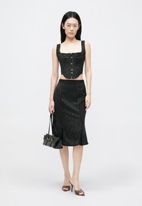 Top corto a rayas negras con cuatro botones, acompañado de una falda lápiz hasta la rodilla y un pequeño bolso negro, con una textura suave.