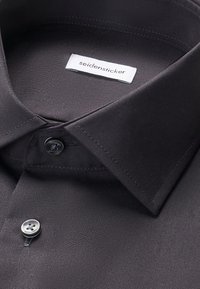 Zbliżenie kołnierzyka czarnej koszuli wizytowej z dwoma guzikami i metką marki "seidensticker" wewnątrz kołnierzyka.