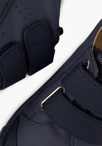 Námořnické modré boty vyrobené z syntetického materiálu s texturovanými suchými zipy a kovovými akcenty. Oválná špička a robustní design podrážky.