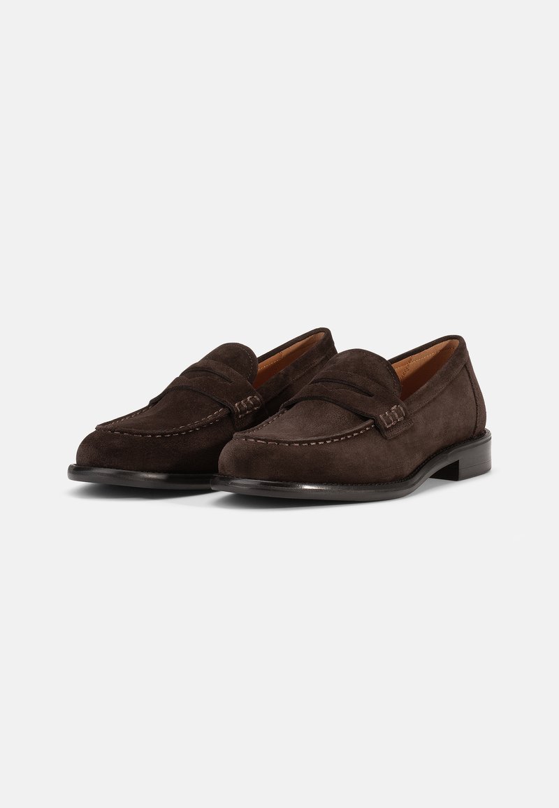 Bruine suède instappers met een gestikt moccasinontwerp, platte leren zool en een verhoogde naad over de wreef voor extra detail.