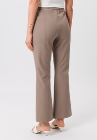 Beige hoge taille broeken met wijde pijpen, een gladde textuur, decoratieve stiksels en een elastische tailleband. Witte open hakken zichtbaar.