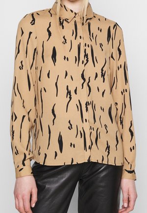 Beige langærmet bluse med sorte abstrakte vertikale mønstre, båret uden at være stoppet ned over sorte læderbukser.