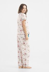 Conjunto de pijama con estampado de estrellas colorido en tela suave. Parte superior de manga corta con cuello y pantalones largos, con cinturilla ajustable y acentos azules.