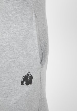 Grijze sweatpants hebben een zwart gorilla-logo op de rechterheup, gemaakt van een zachte katoenmix met een gladde textuur.