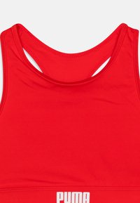 Crvena sportska grudnjak napravljena od glatkog materijala. Ima oblikovano izrezivanje i dizajn s trakama. Istaknuti bijeli "PUMA" logo na elastičnoj traci.