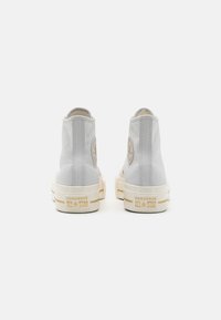 Zapatillas altas de lona gris con suelas de goma blanco roto. Presentan un logotipo grabado en el talón y un emblemático símbolo de estrella.