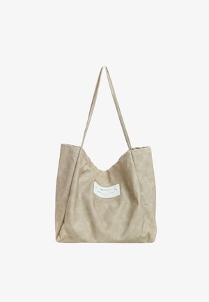 Bolso tote de cuero suave beige con asas largas y una pequeña etiqueta blanca curvada centrada en el frente.