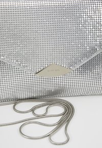 Pochette en maille métallique argentée de style enveloppe avec une fine chaîne argentée, sur fond blanc.