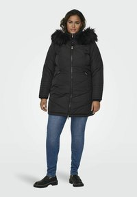 Melna quiltota parka ar mākslīgo kažokādu apšuvumu kapucē, ar rāvējslēdzēju priekšā un sānu kabatām. Iezīmē ribotās piedurknes un garāku siluetu.