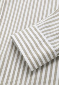 Stribet stofskjorte med horisontale hvide og lyse beige striber, med en rullet manchet der fremviser lignende striber og en tekstureret finish.