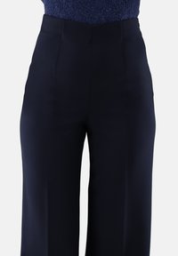 Marineblaue, maßgeschneiderte Hosen aus glattem Stoff, mit hohem Bund und geraden Beinen, die über minimale Nahtdetails verfügen.